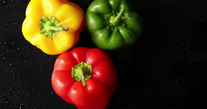 From above view of three bright fresh peppers of different color laid on black background covered with drops