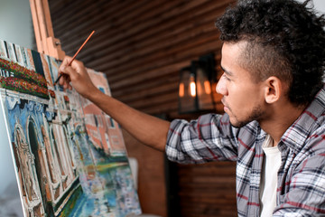 Young African-American artist painting picture in workshop