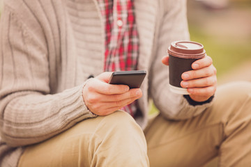Attractive man using cellphone and drinking coffee outdoors.