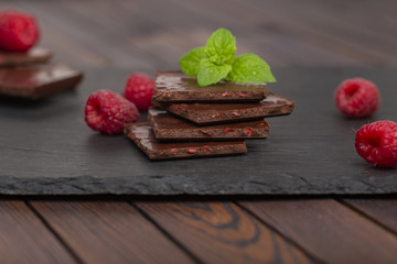 Chocolate with pieces of dry raspberries and fresh raspberries with a mint leaf on a slate plate. Close up.