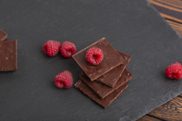 Chocolate with pieces of dry raspberries and fresh raspberries on a slate plate. Close up.