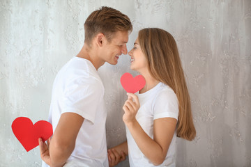 Happy young couple with red hearts near grey wall