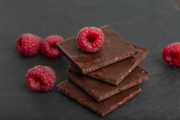 Chocolate with pieces of dry raspberries and fresh raspberries on a slate plate. Close up.