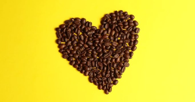 From above view of coffee beans laid in shape of heart on yellow background