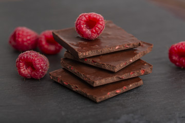 Chocolate with pieces of dry raspberries and fresh raspberries on a slate plate. Close up.