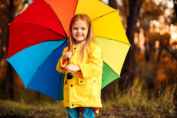 Funny cute toddler girl wearing waterproof coat with colorful umbrella playing in the garden by...