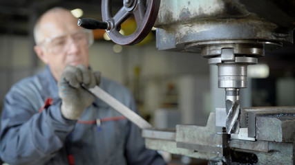 old master is working in a workshop of plant, controlling drilling machine, processing metal details