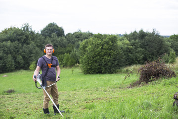 Man takes the grass off with a string gas trimmer