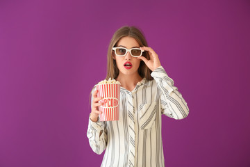 Emotional young woman with cup of popcorn and 3D cinema glasses on color background