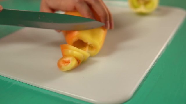 female slices yellow bell pepper. side view of a woman preparing dinner.
