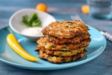 Plate with tasty zucchini pancakes on wooden table, closeup
