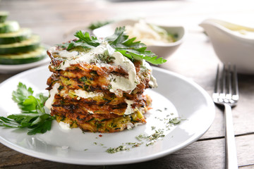 Plate with tasty zucchini pancakes on wooden table, closeup