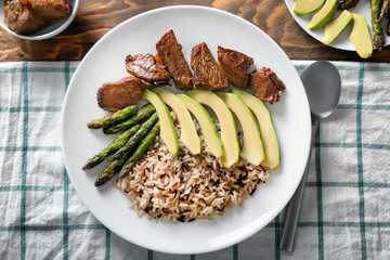 Plate with boiled rice, vegetables and meat on table