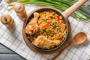 Frying pan with delicious boiled rice, chicken legs and vegetables on wooden board
