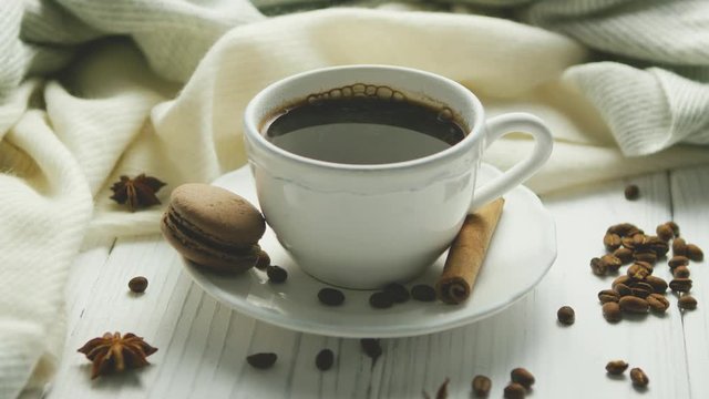 White elegant cup on saucer filled with black coffee and composed on white wooden table with spices