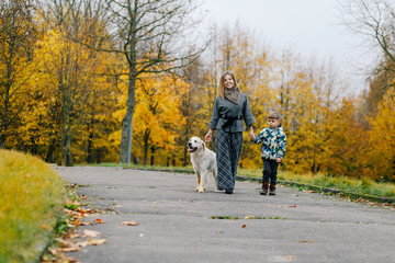 Fototapeta premium Mom and son walking their dog in the park in the fall