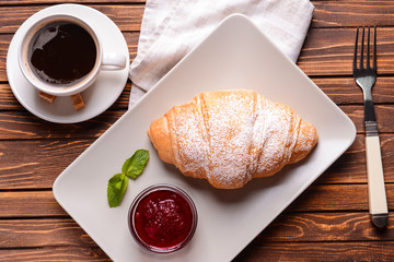 Tasty croissant with jam and cup of coffee on wooden table
