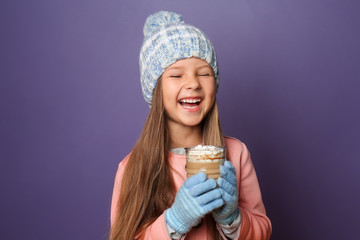 Cute little girl in warm clothes and with glass of hot chocolate on color background