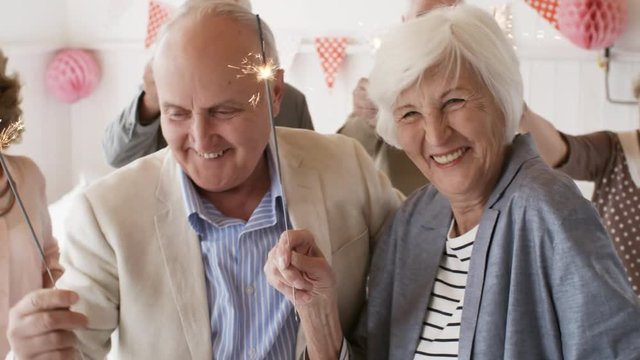 Laughing senior woman and man dancing together with sparklers while having fun with friends at party