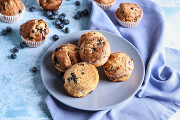 Plate with tasty blueberry muffins on color table