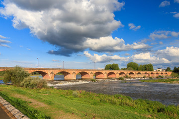 Fototapeta na wymiar Beautiful summer view of the arched bridge over the river Loire (Pont de Loire) in Nevers, France, with a blue sky with clouds
