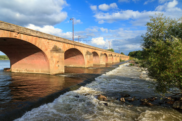 Fototapeta premium Beautiful summer view of the arched bridge over the river Loire (Pont de Loire) in Nevers, France, with a blue sky with clouds