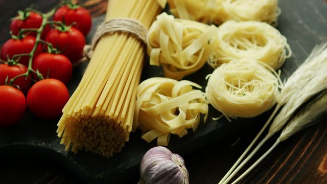 Closeup of uncooked bunch of spaghetti and pasta on board with red tomatoes and garlic