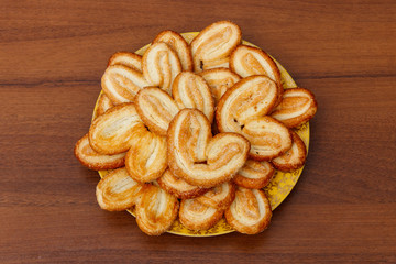 Palmier biscuits - french cookies made of puff pastry (also called palm leaves, elephant ears or french hearts) in a plate on wooden table