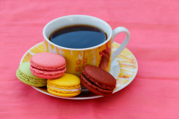 Cup of coffee with tasty colorful macarons on pink background
