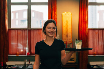 frontal view of a cheerful brunette barista holding a tray with a drink