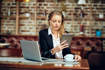 Businesswoman using tablet while sitting in cafeteria. On table laptop and coffee.