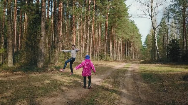 Mother and daughter morning workout in the forest. Woman and girl are running one by one in a spring pine forest, jumping and smiling. Healthy lifestyle