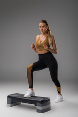 sportive young woman working out on step aerobics board on grey - obrazy, fototapety, plakaty