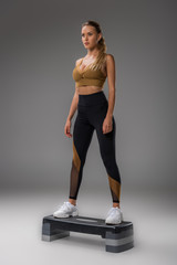 attractive young woman doing step aerobics on grey