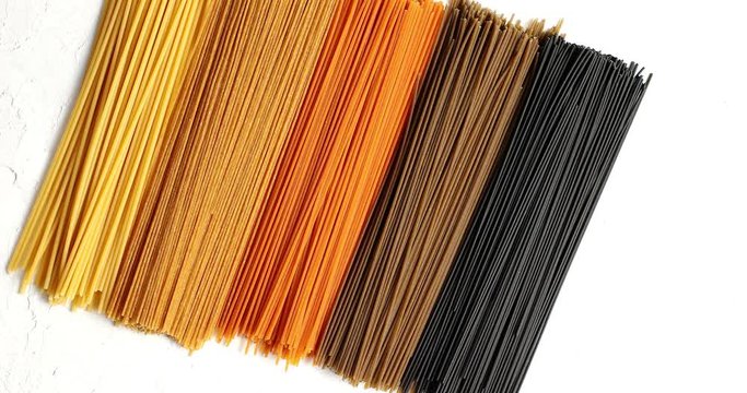 Top view of bunches of uncooked spaghetti of different natural colored lying in row on white background