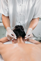 cropped shot of cosmetologist putting needles on womans body during acupuncture therapy in spa salon