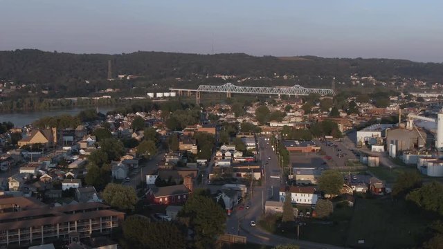 A long orbiting cinematic aerial establishing shot of a small town on the Ohio River in western Pennsylvania at dusk. Pittsburgh suburbs.  
