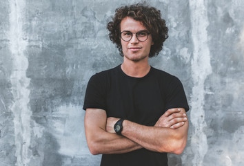 Horizontal outdoor portrait of handsome male with curly hair, wears sepctacles posing for social...