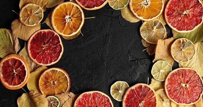 From above shot of arranged wreath on black surface with dry leaves and dry citrus slices
