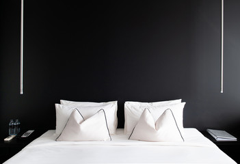 Bedroom with black wall white bed, pillows modern side table, lamp. Modern urban interior