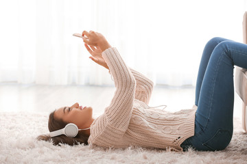 Beautiful young woman listening to music while lying on carpet at home