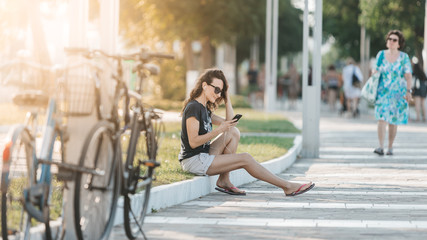Young beautiful happy woman sitting on the lawn with smartphone and headphones listening music or audio book / talking or chatting on mobile phone / warm autumn or summer image