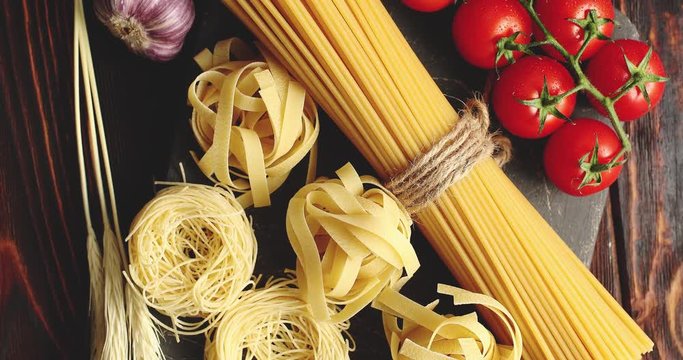 Top view of uncooked mix of pasta and spaghetti on board with grapevine tomatoes and garlic bulb