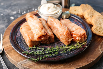 Plate with stuffed cabbage leaves and bowl of sour cream on wooden board