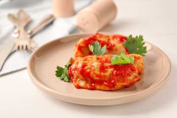 Plate with stuffed cabbage leaves in tomato sauce on white table