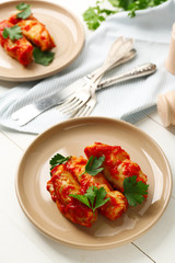 Plate with stuffed cabbage leaves in tomato sauce on white table