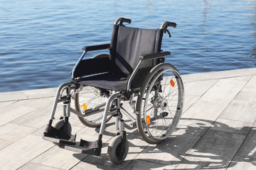 Empty modern wheelchair near river on embankment