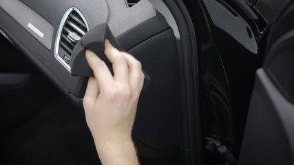 man is cleaning control panel inside a car, rubbing it by soft cloth, removing dust and dirt, close-up