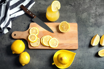 Composition with cutting board, glass of fresh lemon juice and squeezer on grey background