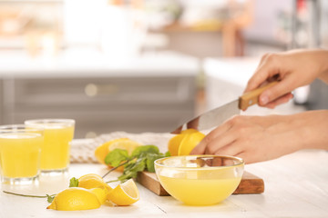 Obraz na płótnie Canvas Woman cutting fresh lemon for juice at table